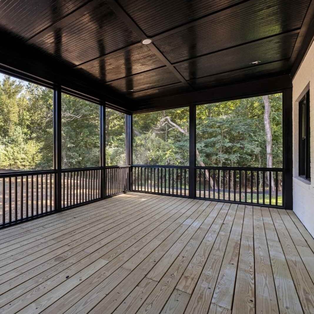 Screened-in patio cover with wood flooring and black railing in Irving, TX backyard