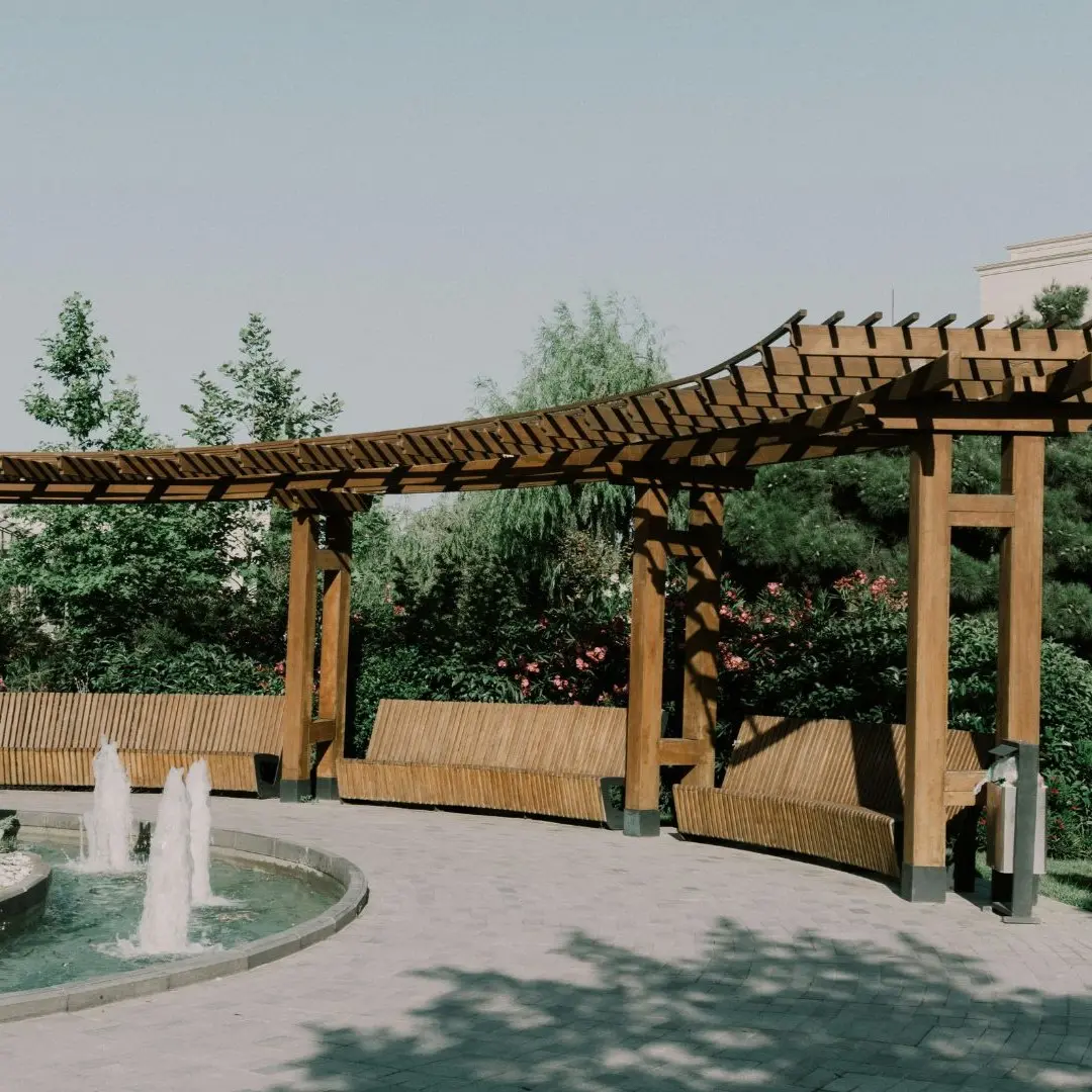 Curved wood pergola with built in benches beside fountains in Highland Village TX