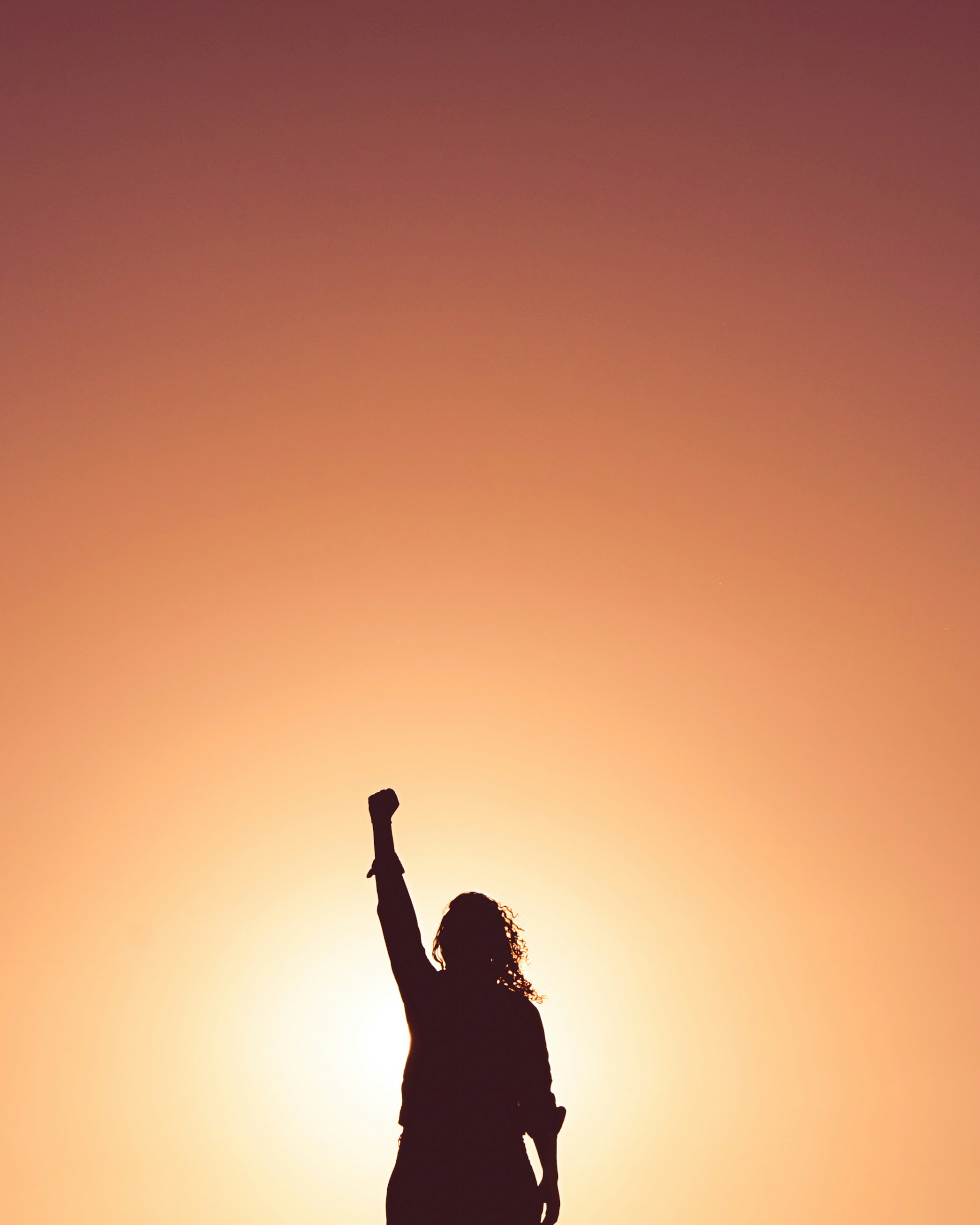 Woman with arms raised in sunset silhouette.