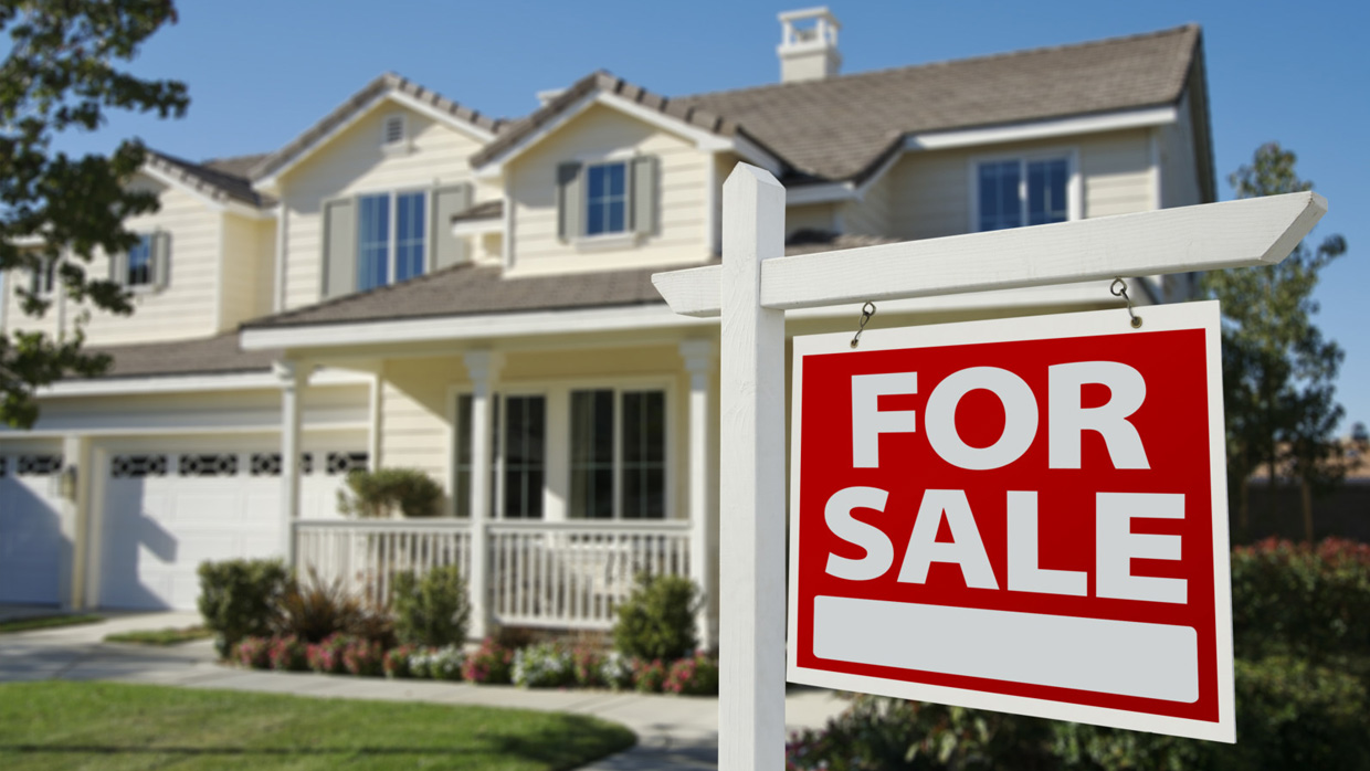 A suburban home with a "For Sale" sign in the front yard, symbolizing the emotional and logistical challenges families face when selling a loved one’s house during a senior transition.