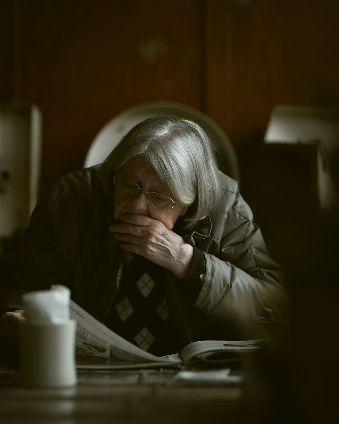 An elderly woman gazes out with a worried expression, symbolizing the emotional burden seniors face when home becomes unsafe and access to care feels out of reach