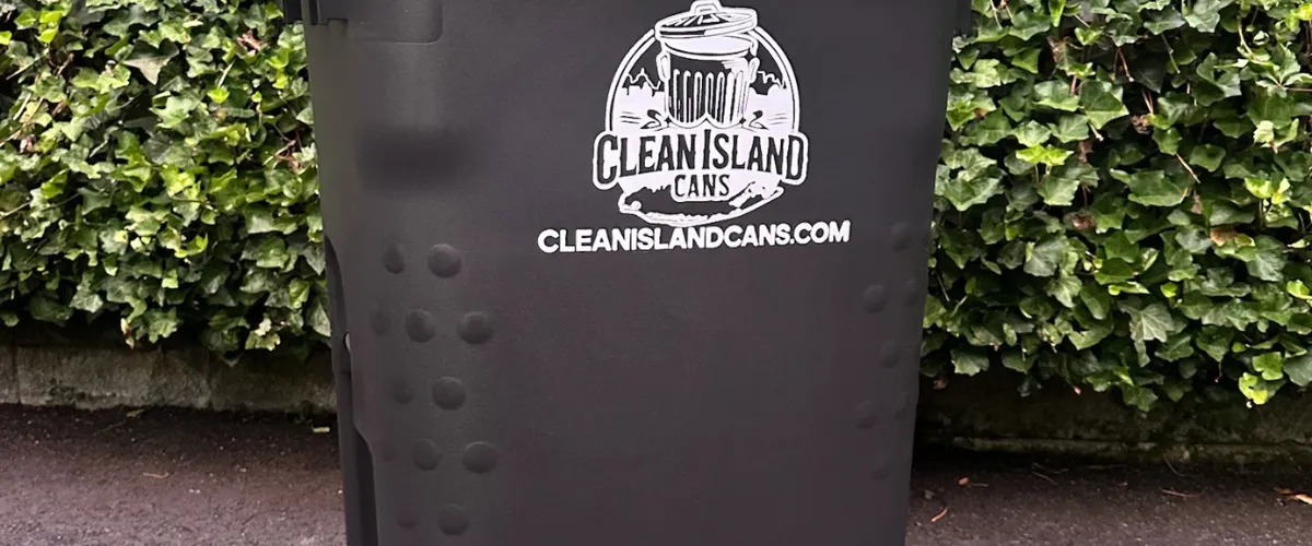 Close-up of Clean Island branded trash bin placed outdoors near green hedge Close-up of Clean Island branded trash bin placed outdoors near green hedge