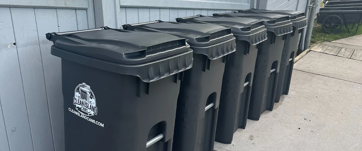 Row of clean black trash bins lined up along a wooden fence. Row of clean black trash bins lined up along a wooden fence.