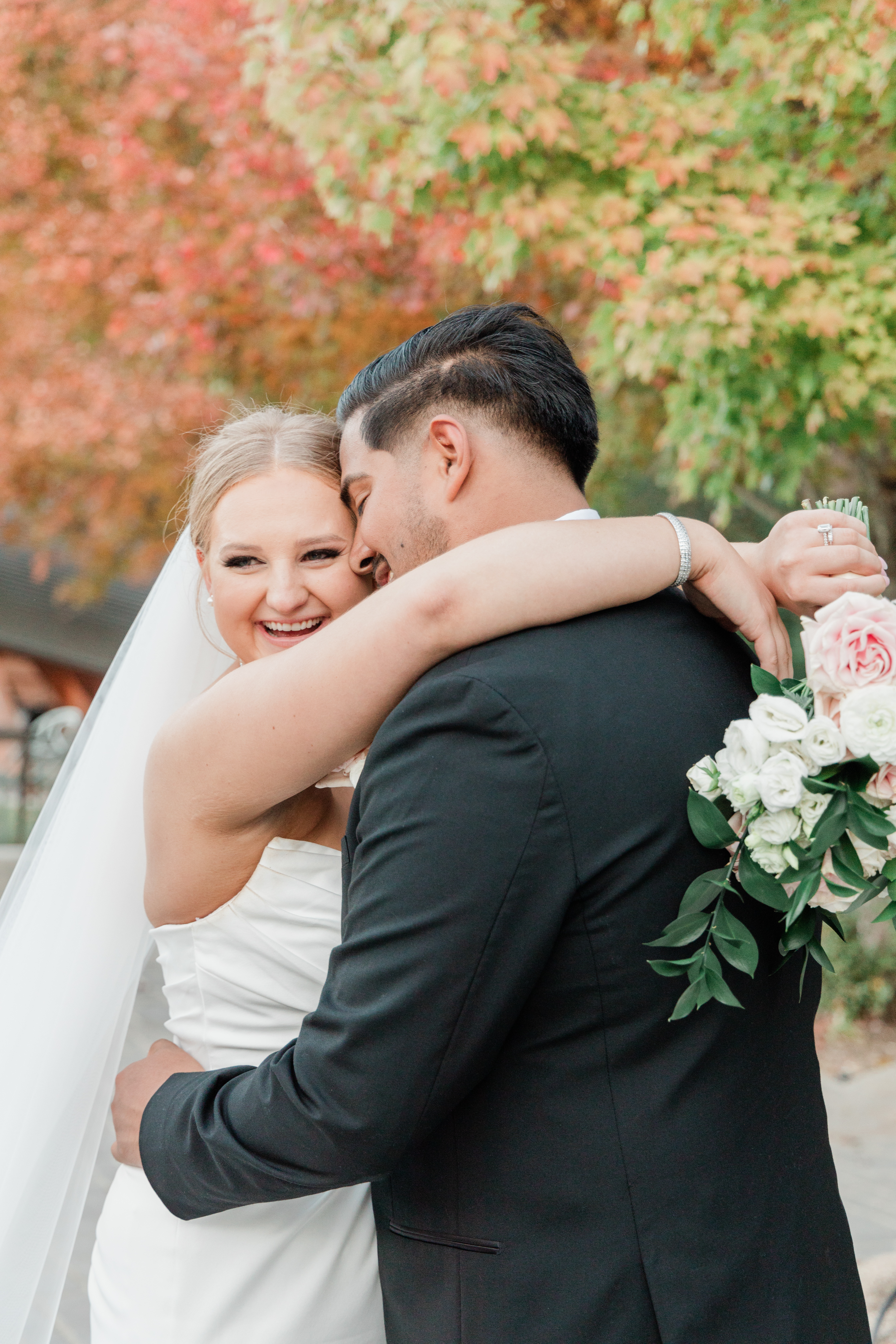 A joyful bride and groom share an intimate forehead-to-forehead moment by the lake, radiating love and elegance. Her pearl-draped top and softly gathered skirt shimmer with quiet luxury, while his tailored beige suit adds timeless refinement. Captured by Seattle wedding photographer Adina Stiles, this image evokes the polished intimacy and enduring style of a true heirloom.