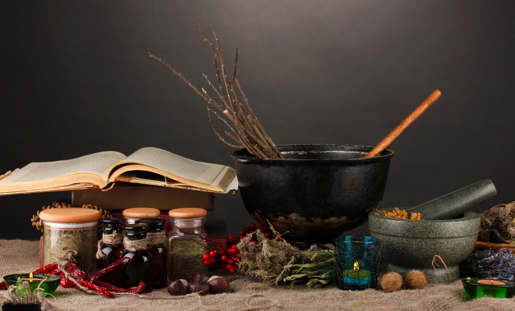 A witch's cauldron sits on a table with books and various ingredients A witch's cauldron sits on a table with books and various ingredients