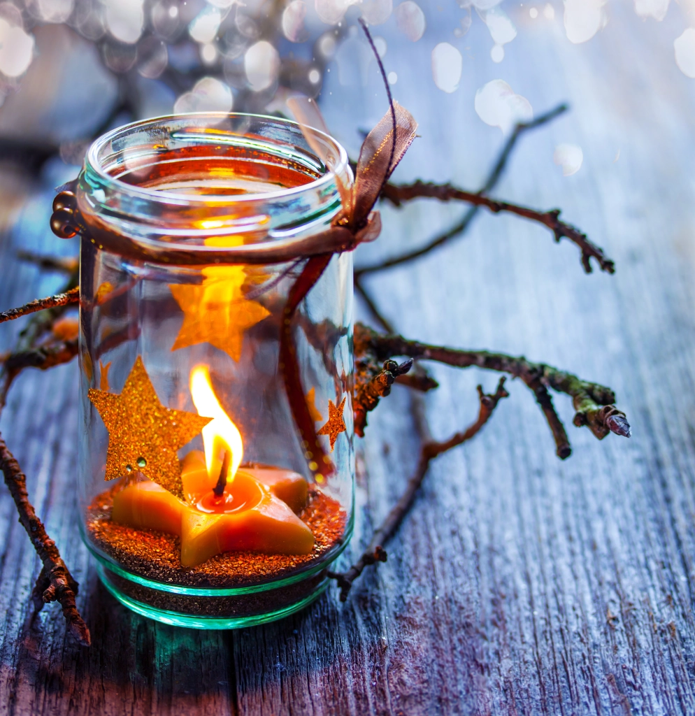 A jar sits on a table with a lit star candle inside of it A jar sits on a table with a lit star candle inside of it