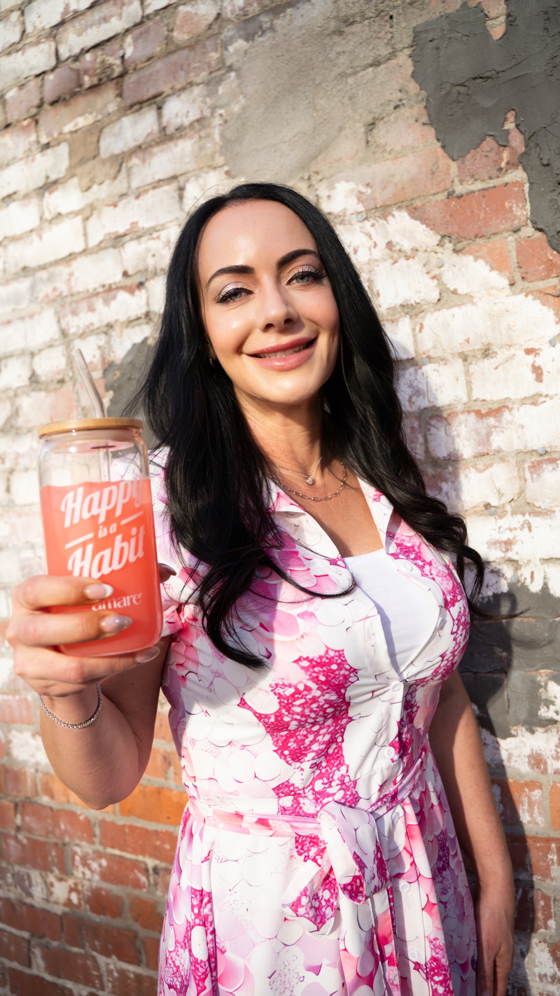 Jen Sells smiling in a pink and white dress, holding Happy Juice in front of a red brick wall, lifestyle wellness image for Inspiring You blog. Jen Sells smiling in a pink and white dress, holding Happy Juice in front of a red brick wall, lifestyle wellness image for Inspiring You blog.