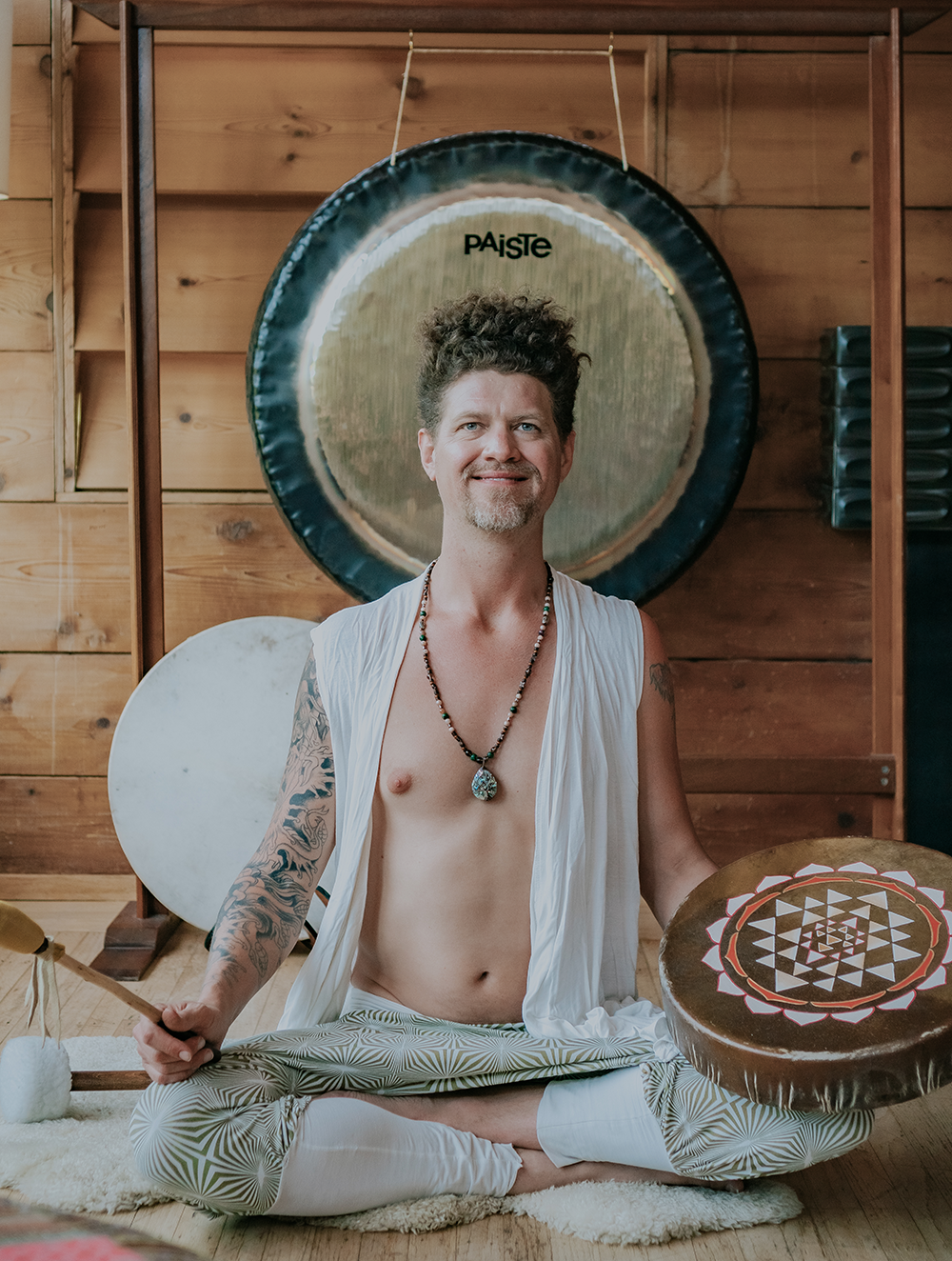 Man meditating in front of a gong with ceremonial drum and mallet during a sound healing session Man meditating in front of a gong with ceremonial drum and mallet during a sound healing session