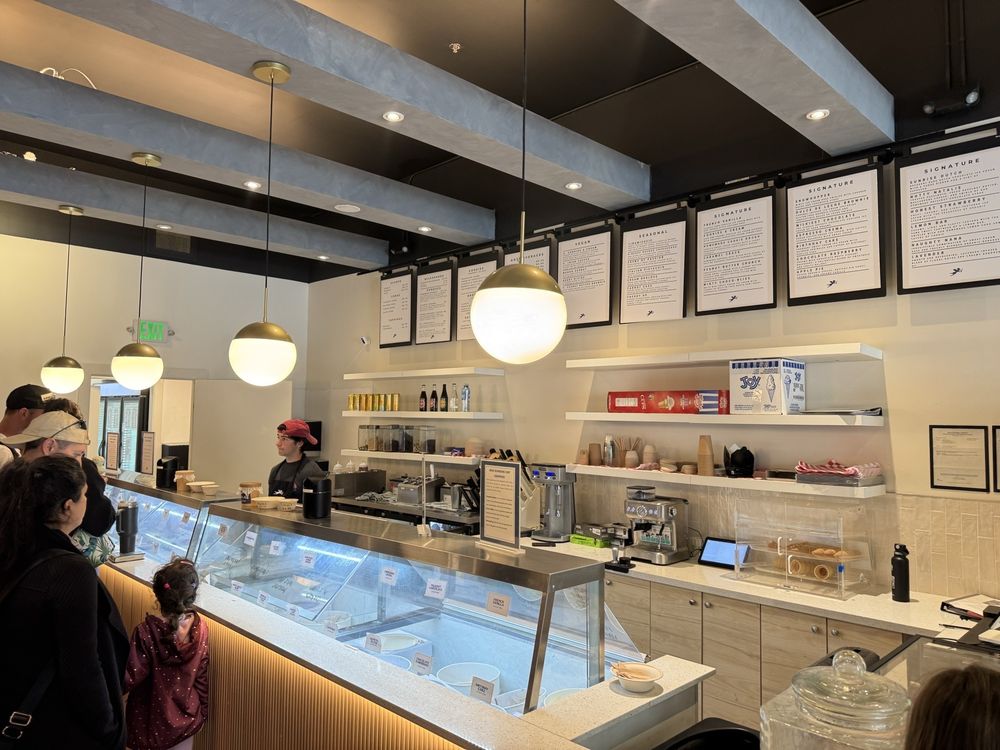 customers line up inside Angela’s Organic Ice Cream Parlor, a cozy space with rustic wooden accents, vintage churning equipment, and a display of homemade, organic ice cream crafted from locally sourced ingredients.