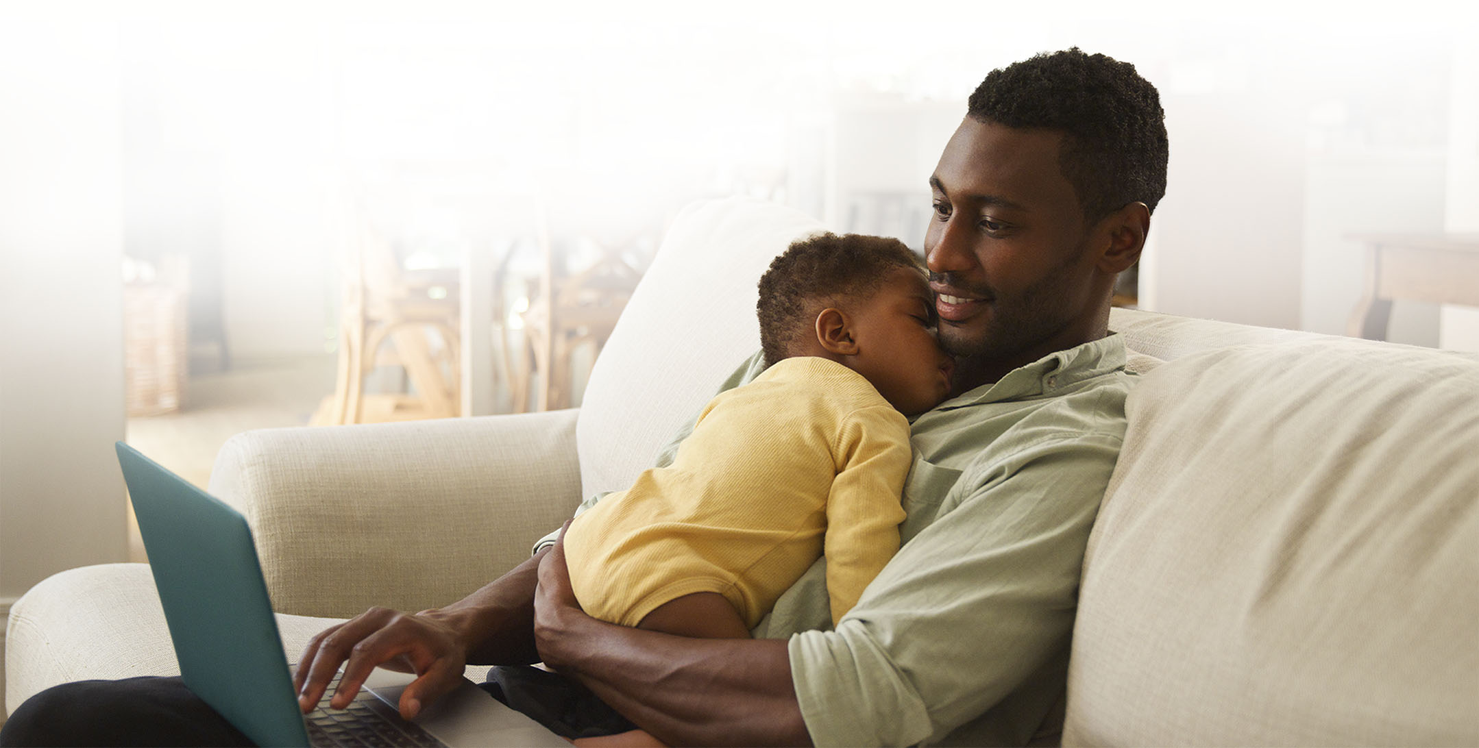 Man holding a baby while working on a laptop at home