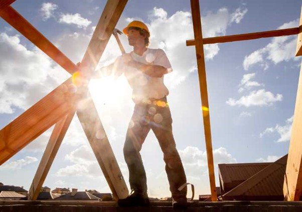 Roofer carpenter working on roof on construction site outdoors with sunflare and blue sky