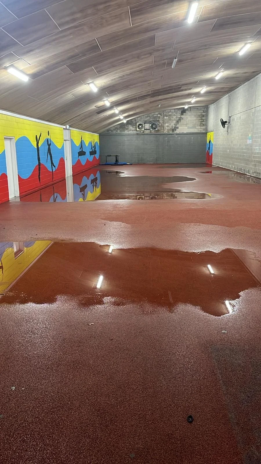 Floodwater covering the gymnasium floor at Sydney Academy of Sport after heavy rain, showing extensive groundwater intrusion and surface contamination. Floodwater covering the gymnasium floor at Sydney Academy of Sport after heavy rain, showing extensive groundwater intrusion and surface contamination.