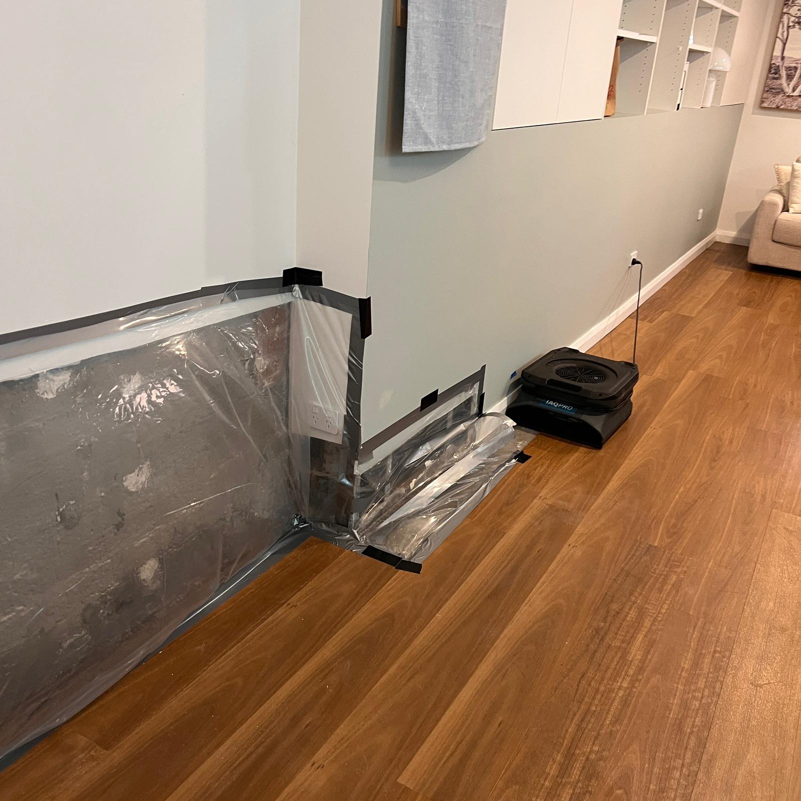 Plastic containment and drying equipment set up along a removed gyprock section to isolate moisture and stabilise humidity during mould remediation inside a residential living area. Plastic containment and drying equipment set up along a removed gyprock section to isolate moisture and stabilise humidity during mould remediation inside a residential living area.