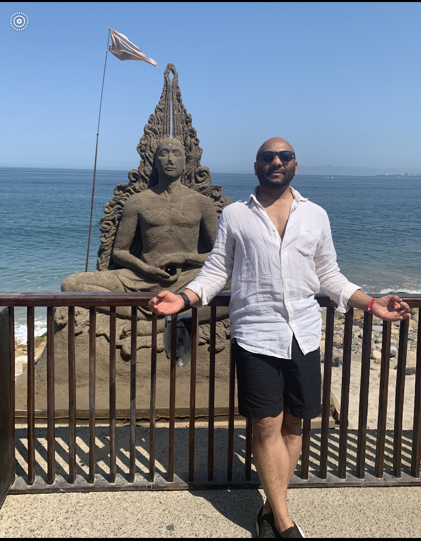 A male fitness coach standing in front of a buddha statue at the beach