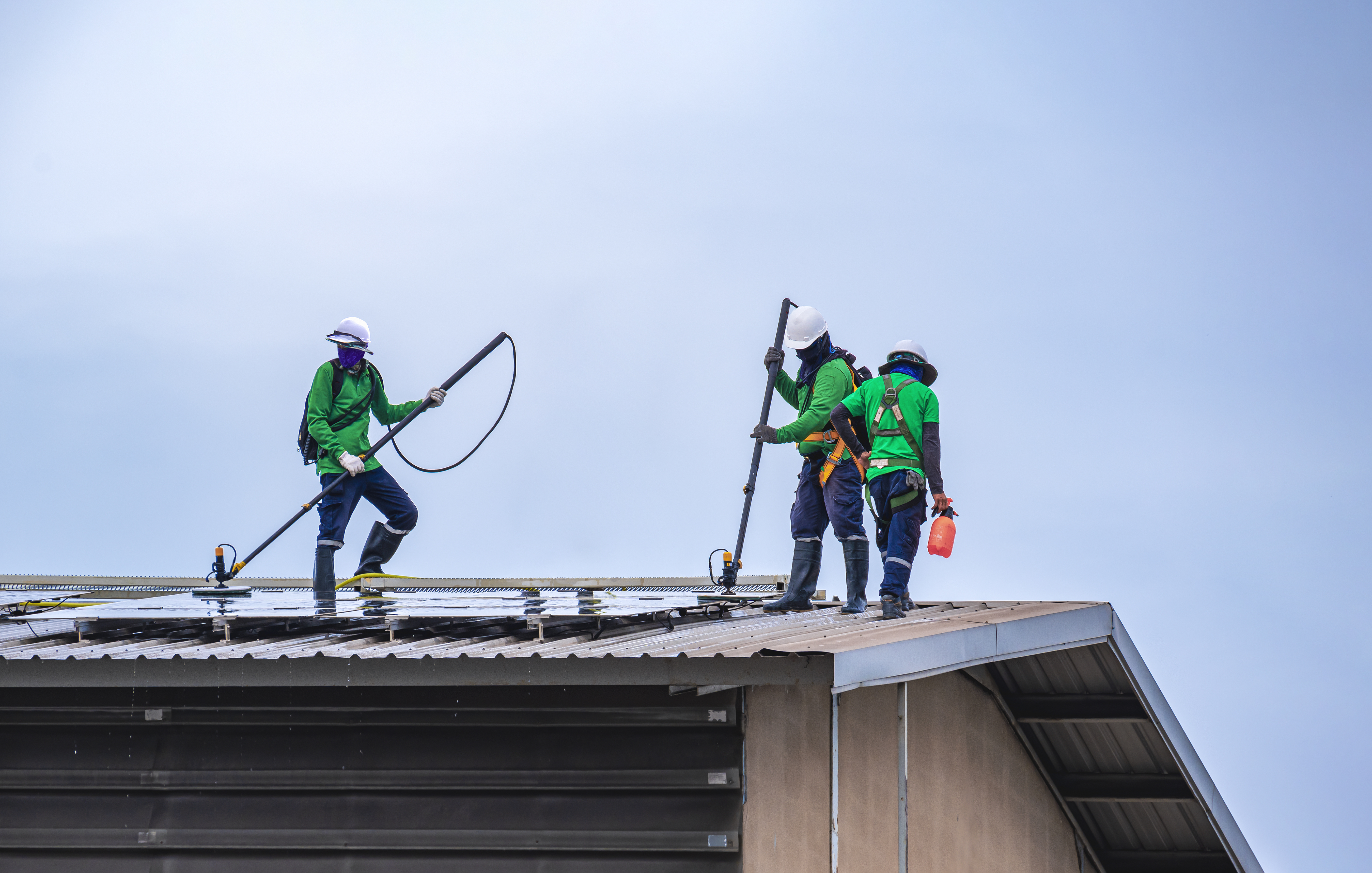 a high-angle view of a bustling roofing project site, featuring workers in bright safety gear and harnesses implementing fall protection systems while carefully navigating a steep roof under a clear blue sky. a high-angle view of a bustling roofing project site, featuring workers in bright safety gear and harnesses implementing fall protection systems while carefully navigating a steep roof under a clear blue sky.