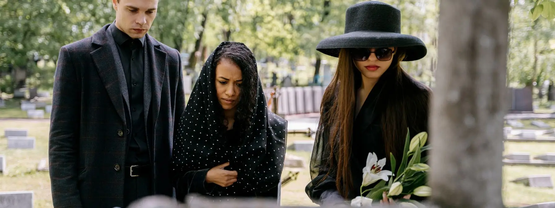 Three mourners dressed in black stand solemnly at a gravesite holding lilies, reflecting the emotional and legal consequences of dying without a will in West Virginia. Three mourners dressed in black stand solemnly at a gravesite holding lilies, reflecting the emotional and legal consequences of dying without a will in West Virginia.