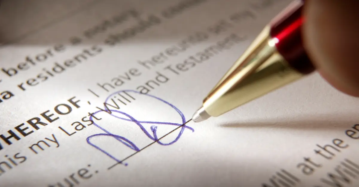 Close-up of a pen signing a legal document titled "Last Will and Testament," with the signature written in blue ink.