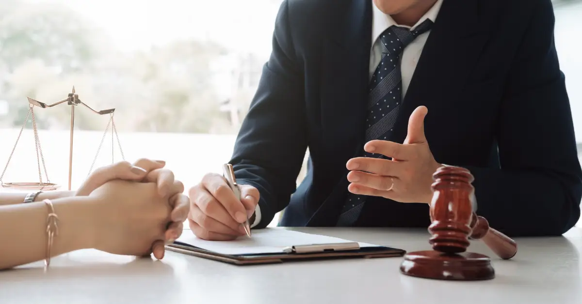 Close-up of a lawyer in a suit discussing legal matters with a client, with a clipboard, gavel, and scales of justice on the table.