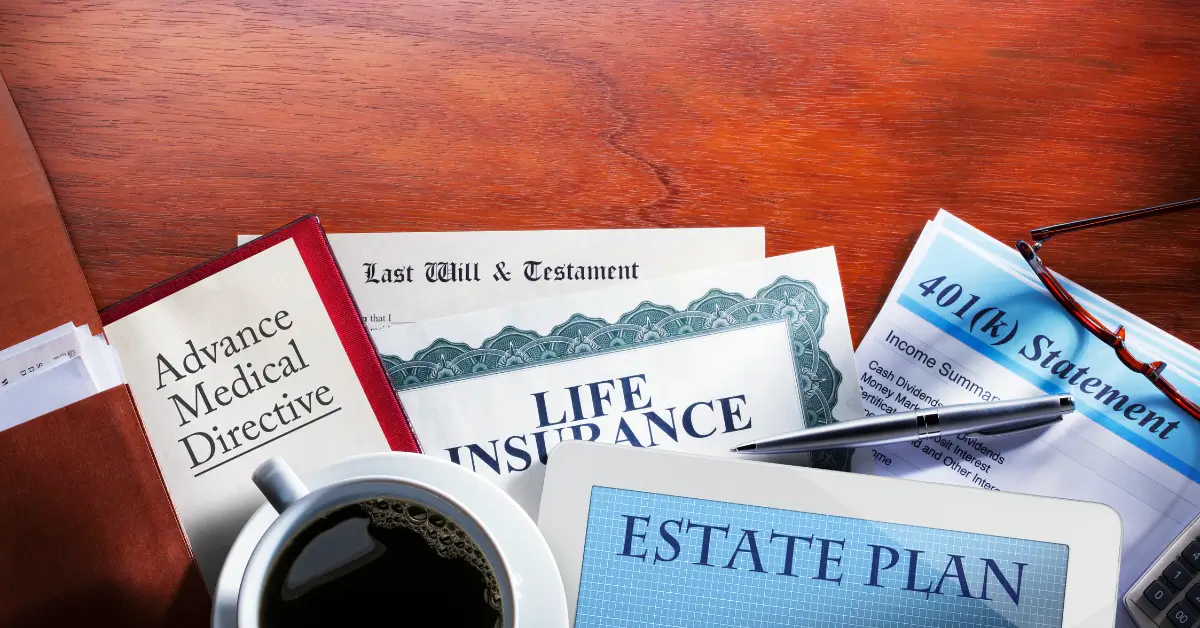 Estate planning documents and related items laid out on a wooden desk, including an Advance Medical Directive, Last Will and Testament, Life Insurance policy, 401(k) statement, a tablet displaying "Estate Plan," a pen, reading glasses, and a cup of coffee.