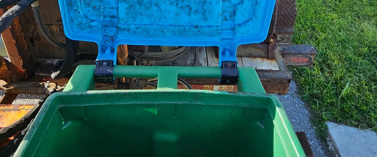 Open green trash bin being lifted toward a trash can cleaning truck Open green trash bin being lifted toward a trash can cleaning truck