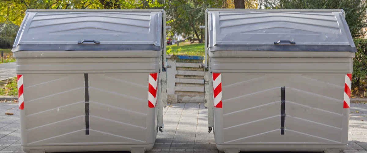 Two large commercial trash containers placed outdoors. Two large commercial trash containers placed outdoors.