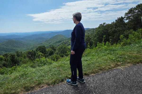 Woman standing on a mountain overlook, gazing at the horizon under a bright sky, symbolizing resilience and hope after loss.
