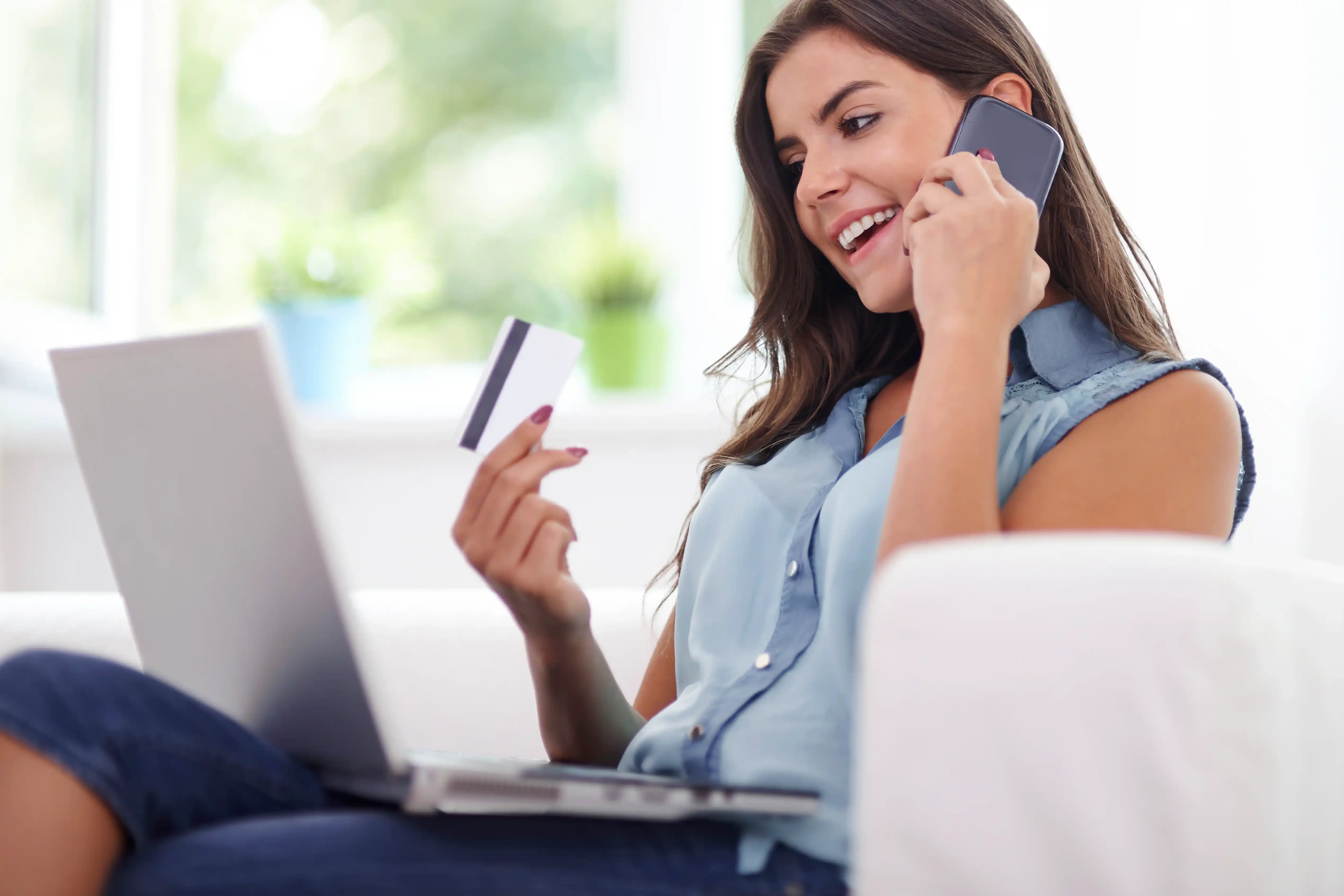 Woman using her laptop and phone while holding a credit card, showing how pay per call supports e-commerce sales Woman using her laptop and phone while holding a credit card, showing how pay per call supports e-commerce sales