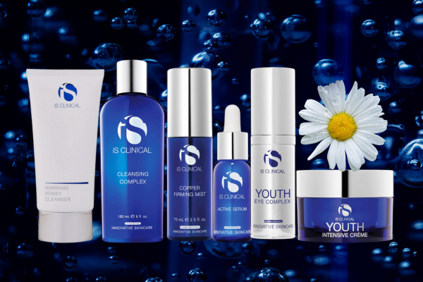 Six IS CLINICAL skincare products arranged in a row against a dark blue background with water bubbles and a white daisy flower. The products include Warming Honey Cleanser, Cleansing Complex, Copper Firming Mist, Active Serum, Youth Eye Complex, and Youth Intensive Creme. Six IS CLINICAL skincare products arranged in a row against a dark blue background with water bubbles and a white daisy flower. The products include Warming Honey Cleanser, Cleansing Complex, Copper Firming Mist, Active Serum, Youth Eye Complex, and Youth Intensive Creme.
