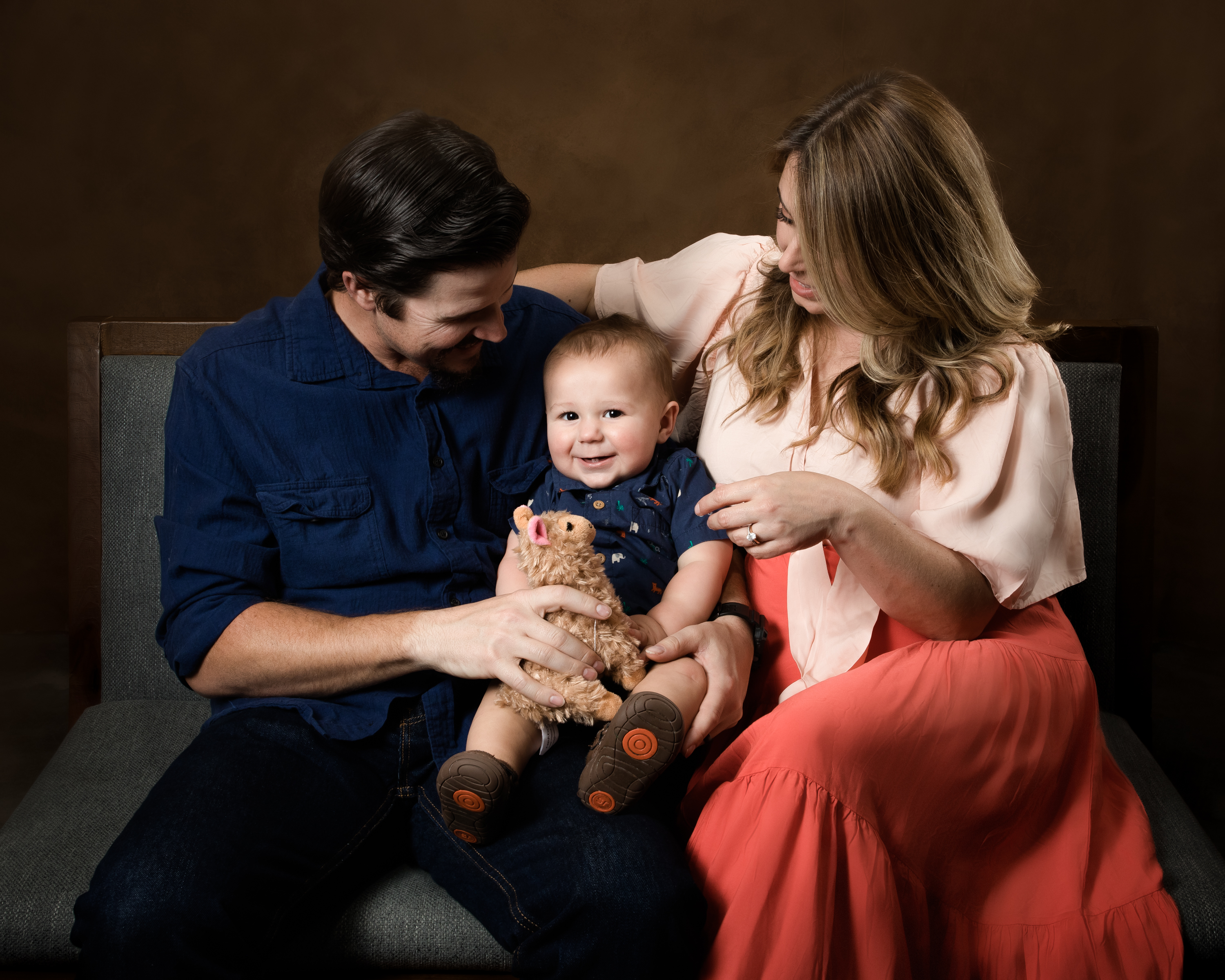 ChatGPT said:  A happy baby sits between loving parents, holding a stuffed animal and smiling brightly. Photographed by Los Angeles photographer Kendra Greenberg Photography.