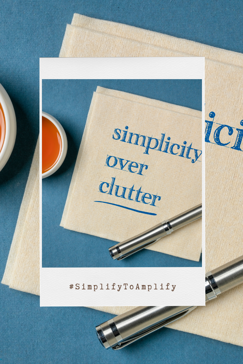 A neatly organized desktop featuring a notebook with the phrase 'simplicity over clutter' printed on the cover, alongside a stylish metal pen and a cup of tea, with the hashtag #SimplifyToAmplify prominently displayed, embodying the essence of organization and focus in the workspace.