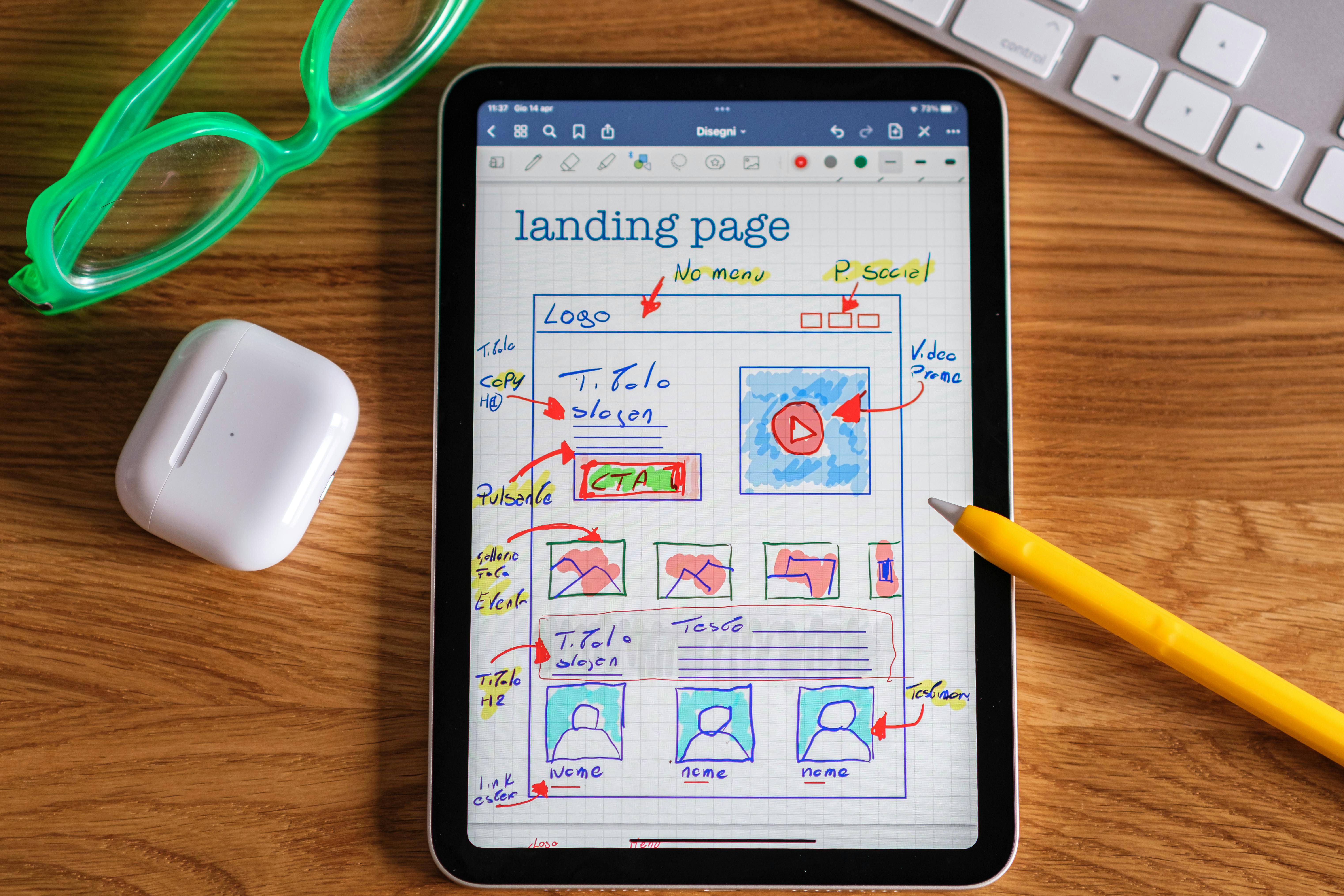 Tablet screen displaying a colorful hand-drawn wireframe of a landing page layout with notes and arrows, surrounded by a yellow pen, green glasses, wireless earbuds case, and a keyboard—representing website planning, UX/UI design, and digital marketing strategy. Tablet screen displaying a colorful hand-drawn wireframe of a landing page layout with notes and arrows, surrounded by a yellow pen, green glasses, wireless earbuds case, and a keyboard—representing website planning, UX/UI design, and digital marketing strategy.