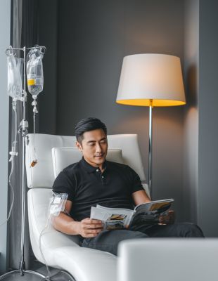 Man receiving an iron IV drip in a modern wellness clinic, reading comfortably during intravenous iron therapy for energy and anaemia support.