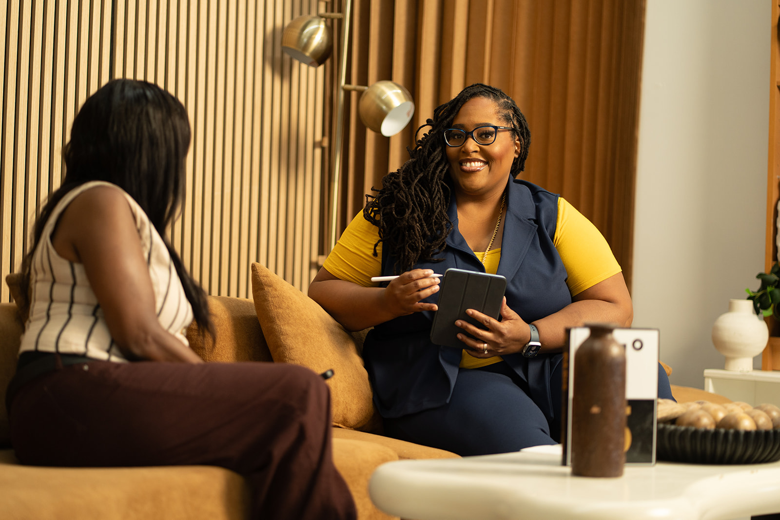 Aimee Nelson and Marsha M. Tate sit on a couch talking Aimee Nelson and Marsha M. Tate sit on a couch talking