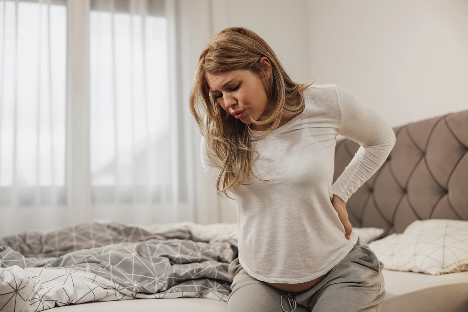 A woman sitting on the bed experiencing back pain