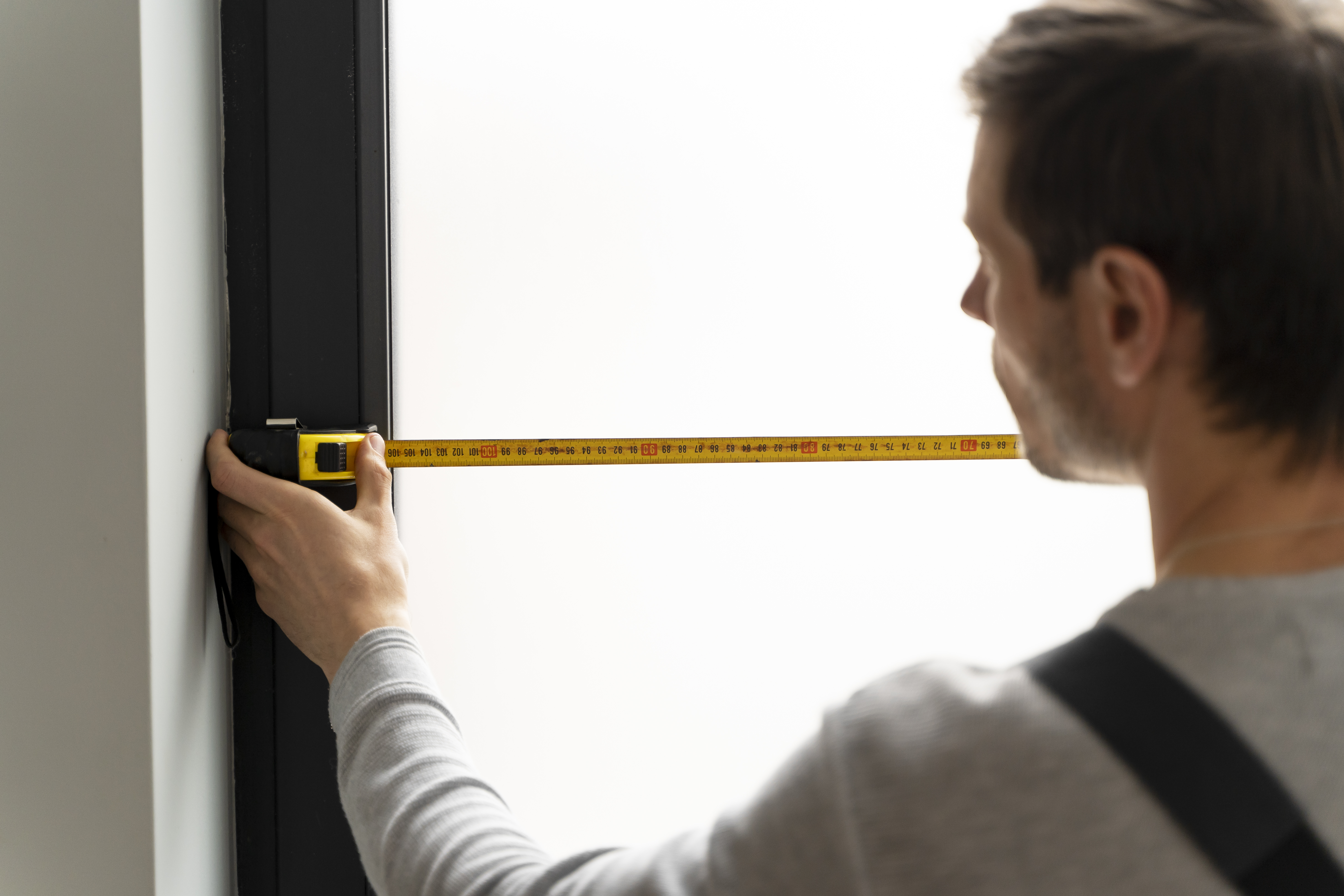 a man with a measuring tape measuring a window a man with a measuring tape measuring a window
