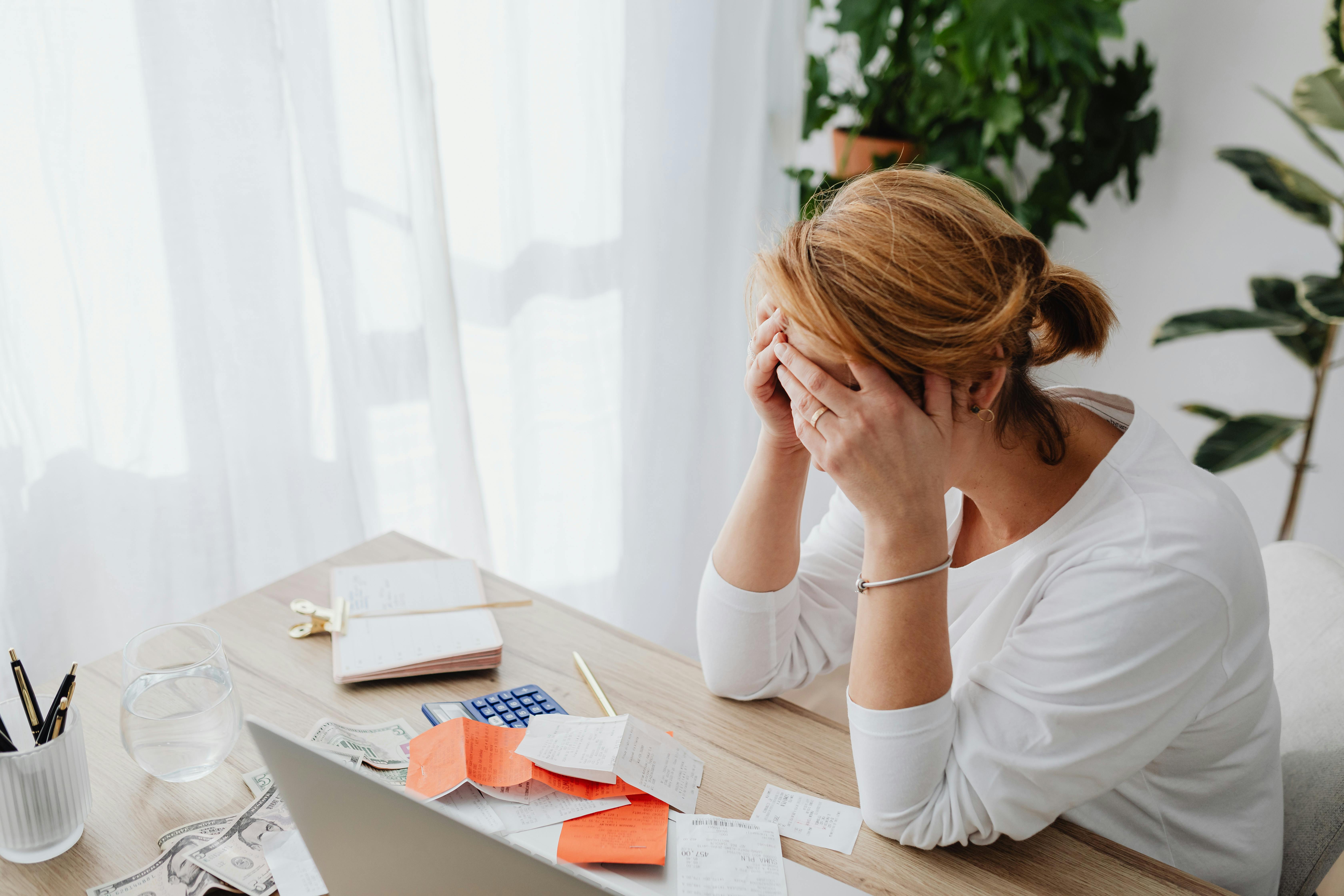 Stressed woman sitting at desk with head in hands, symbolising sleep issues, poor focus, and brain fog linked to mould exposure.
