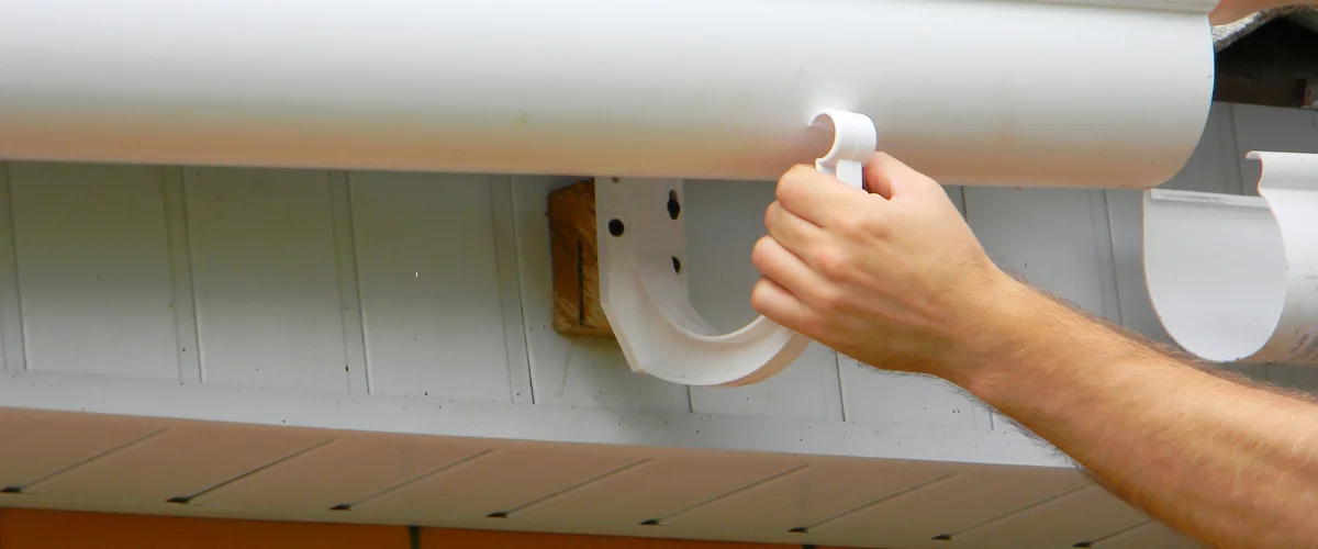 Professional installing white rain gutter on house roof edge