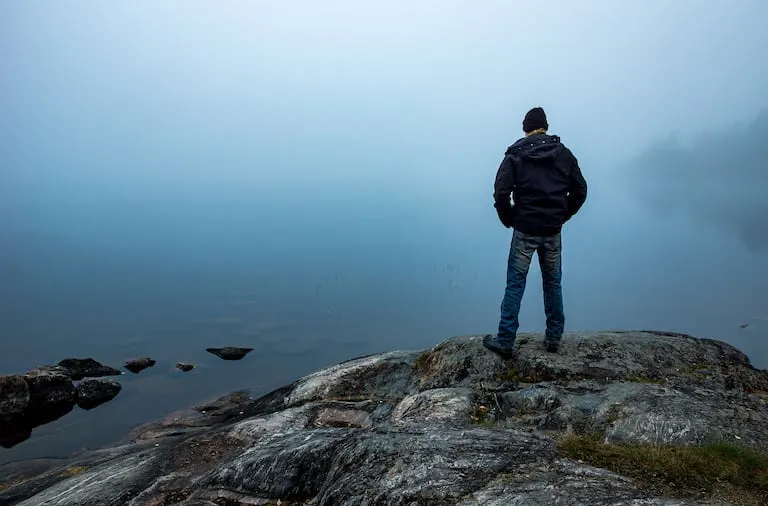 Man standing on a cliff looking into a primordial fog Man standing on a cliff looking into a primordial fog