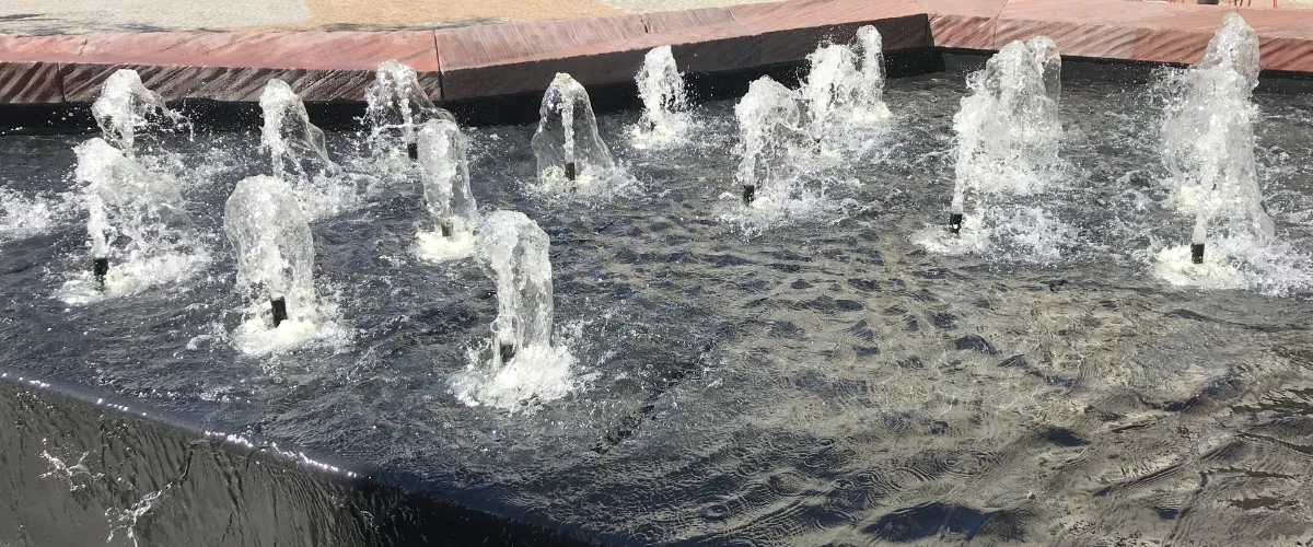Multiple water jets spraying from nozzles in a decorative fountain display.