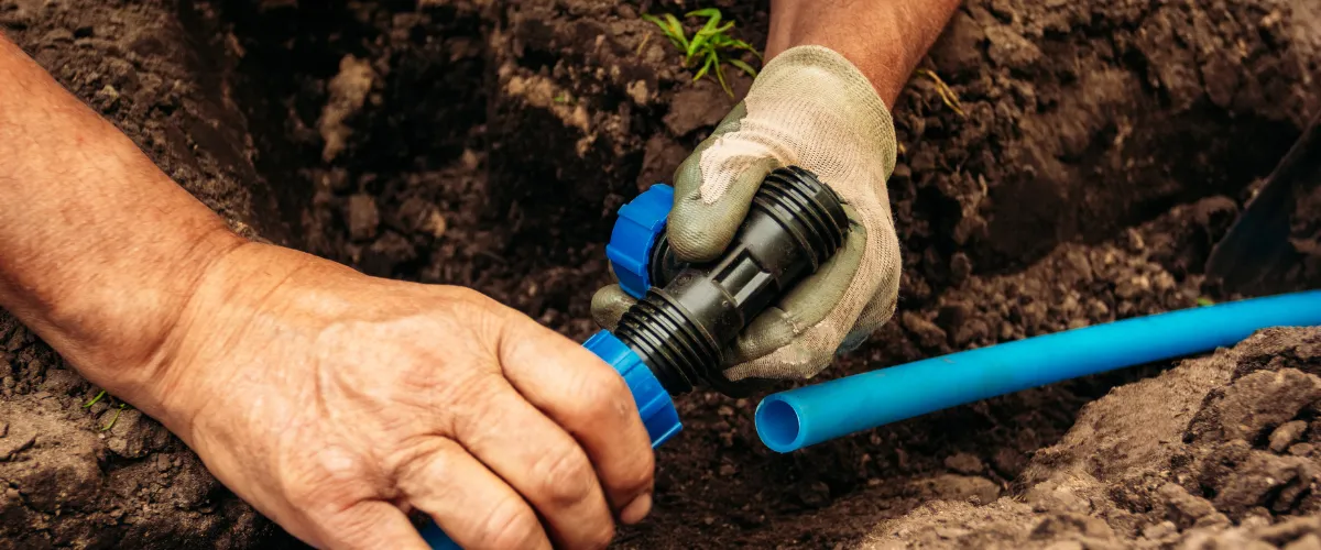 Close-up of hands connecting irrigation pipes for underground water system.
