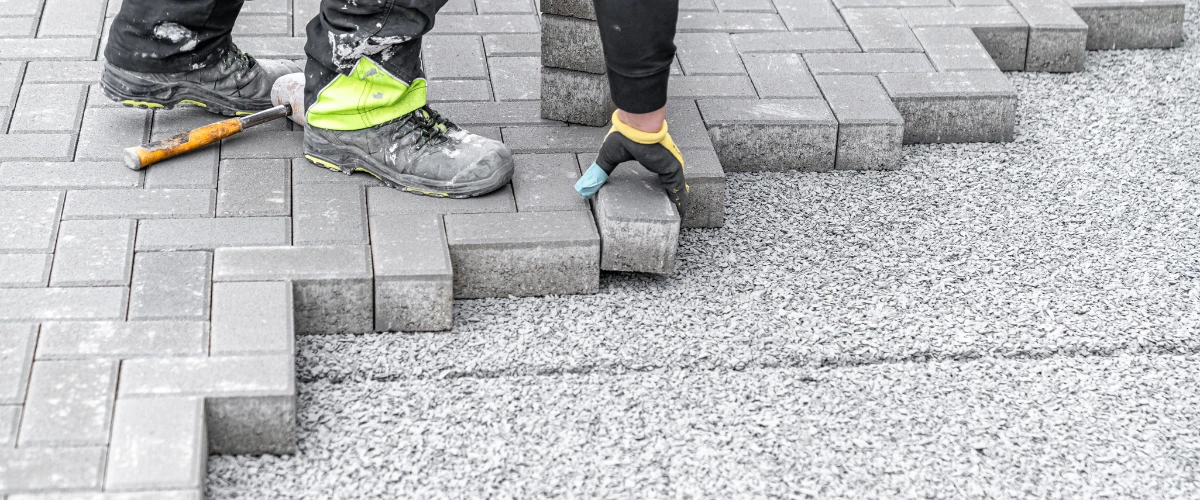 Construction worker laying concrete paving blocks on a prepared gravel surface for a driveway Construction worker laying concrete paving blocks on a prepared gravel surface for a driveway