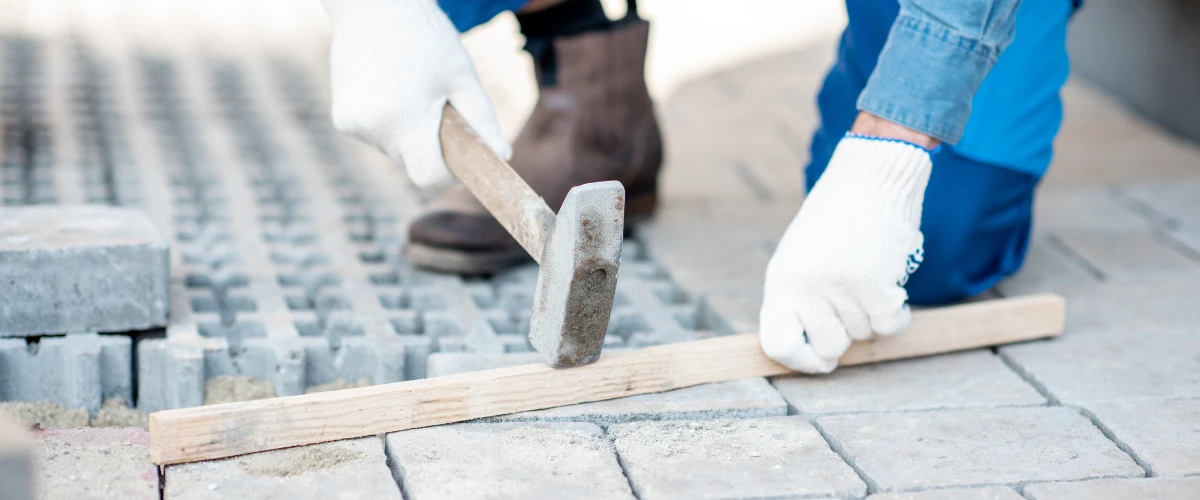 Worker hammering a wooden guide to align paving stones during driveway installation Worker hammering a wooden guide to align paving stones during driveway installation