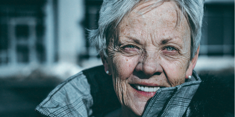 A close-up portrait of an elderly woman with short gray hair and a warm smile, wearing a winter coat. Her face has visible wrinkles, and she appears content, with natural light illuminating her features A close-up portrait of an elderly woman with short gray hair and a warm smile, wearing a winter coat. Her face has visible wrinkles, and she appears content, with natural light illuminating her features