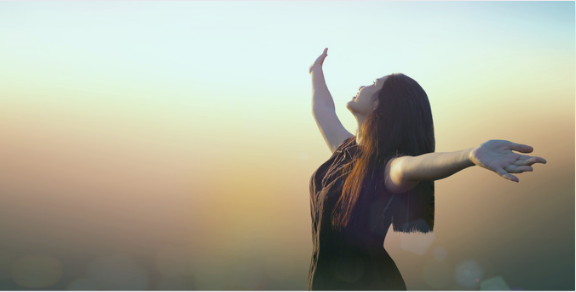 A woman with long hair, wearing a black dress, stands outdoors with her arms wide open and her face lifted towards the sky. The background features a soft, warm-toned sky with a sunset or sunrise effect, symbolizing freedom, joy, and positivity A woman with long hair, wearing a black dress, stands outdoors with her arms wide open and her face lifted towards the sky. The background features a soft, warm-toned sky with a sunset or sunrise effect, symbolizing freedom, joy, and positivity