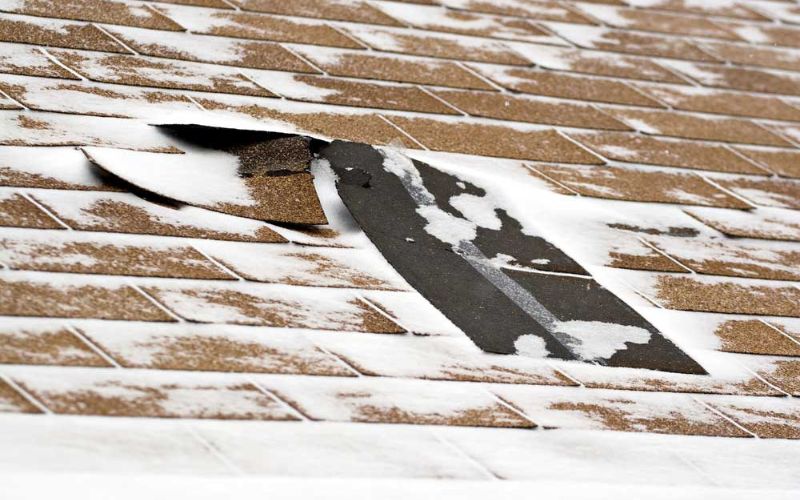 Close-up of a damaged roof with missing shingles and snow accumulation, highlighting the impact of severe weather conditions. Close-up of a damaged roof with missing shingles and snow accumulation, highlighting the impact of severe weather conditions.