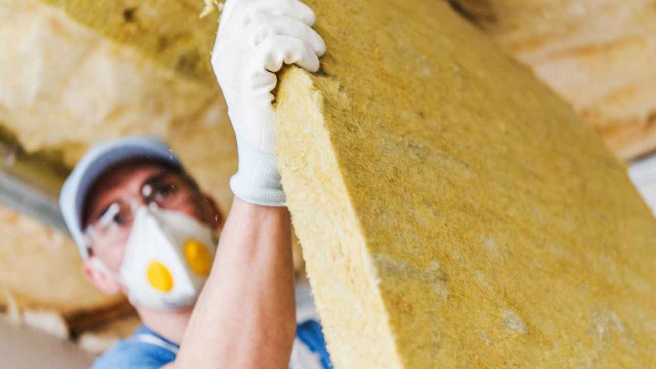 Roofer installing insulation in a roof, wearing protective gloves and a mask for safety during the process Roofer installing insulation in a roof, wearing protective gloves and a mask for safety during the process
