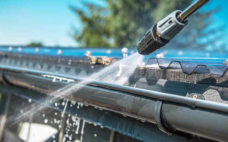 Close-up of a pressure washer cleaning a residential roof gutter with high-pressure water, removing dirt and debris for maintenance and protection against damage. Ideal for home exterior cleaning services and roof maintenance tips. Close-up of a pressure washer cleaning a residential roof gutter with high-pressure water, removing dirt and debris for maintenance and protection against damage. Ideal for home exterior cleaning services and roof maintenance tips.