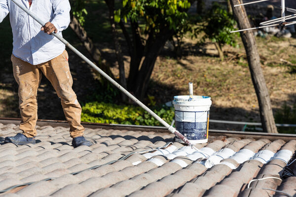 a worker applies roof coating, protecting the surface from weathering and ensuring durability a worker applies roof coating, protecting the surface from weathering and ensuring durability
