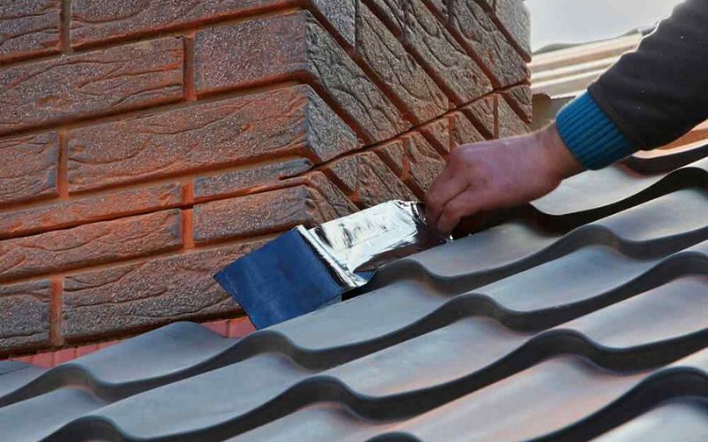 Close-up of a roofer's hand applying flashing tape on a metal roof near a brick chimney to ensure proper sealing and prevent leaks. Close-up of a roofer's hand applying flashing tape on a metal roof near a brick chimney to ensure proper sealing and prevent leaks.