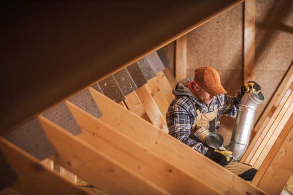 Roofer installing ventilation ducts in an attic, highlighting the importance of proper roof ventilation for energy efficiency and moisture control. Roofer installing ventilation ducts in an attic, highlighting the importance of proper roof ventilation for energy efficiency and moisture control.